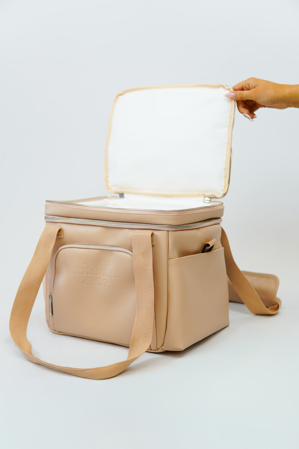 Beige cooler bag with a hand opening the lid on a white background