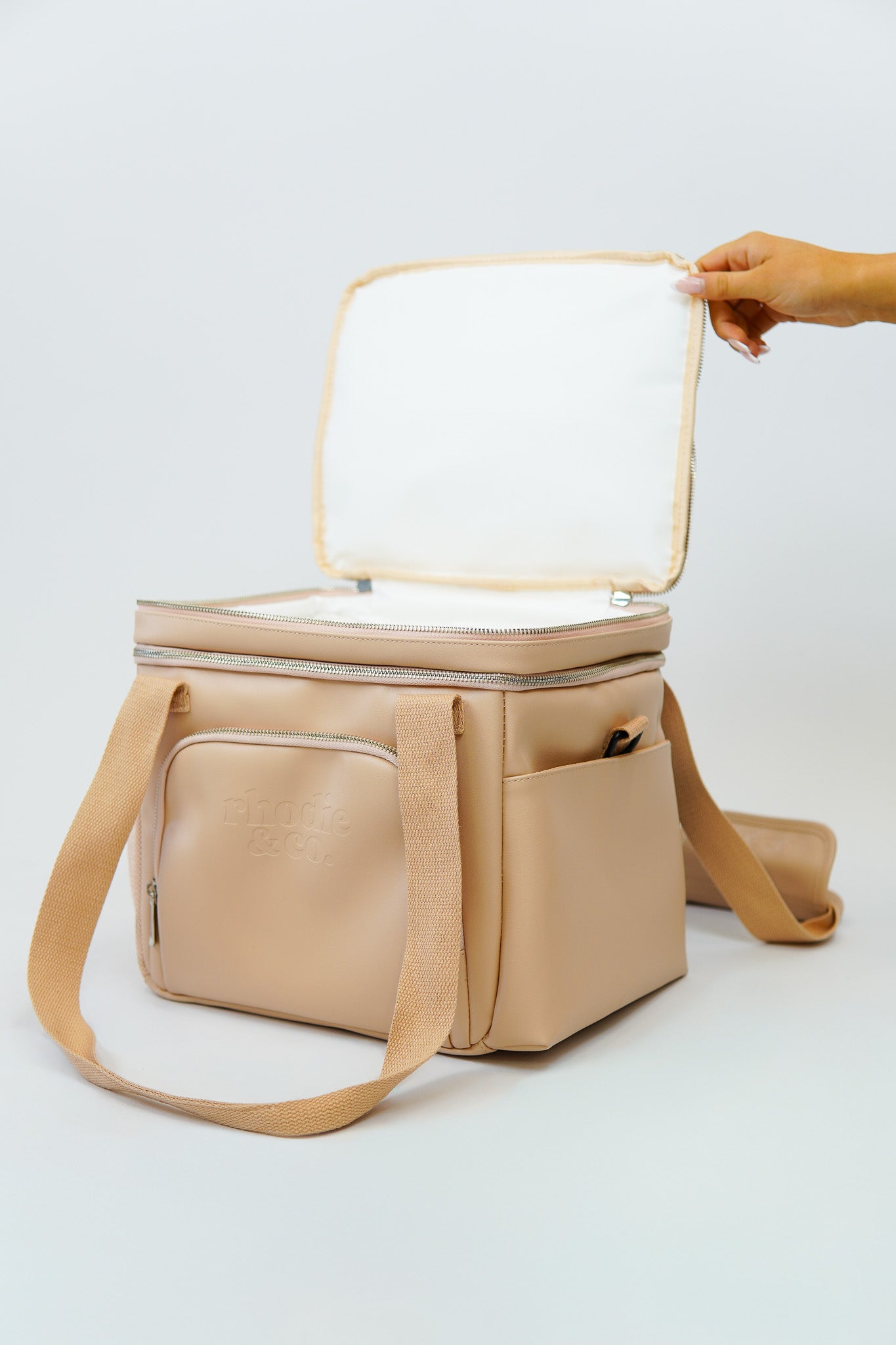 Beige cooler bag with a hand opening the lid on a white background
