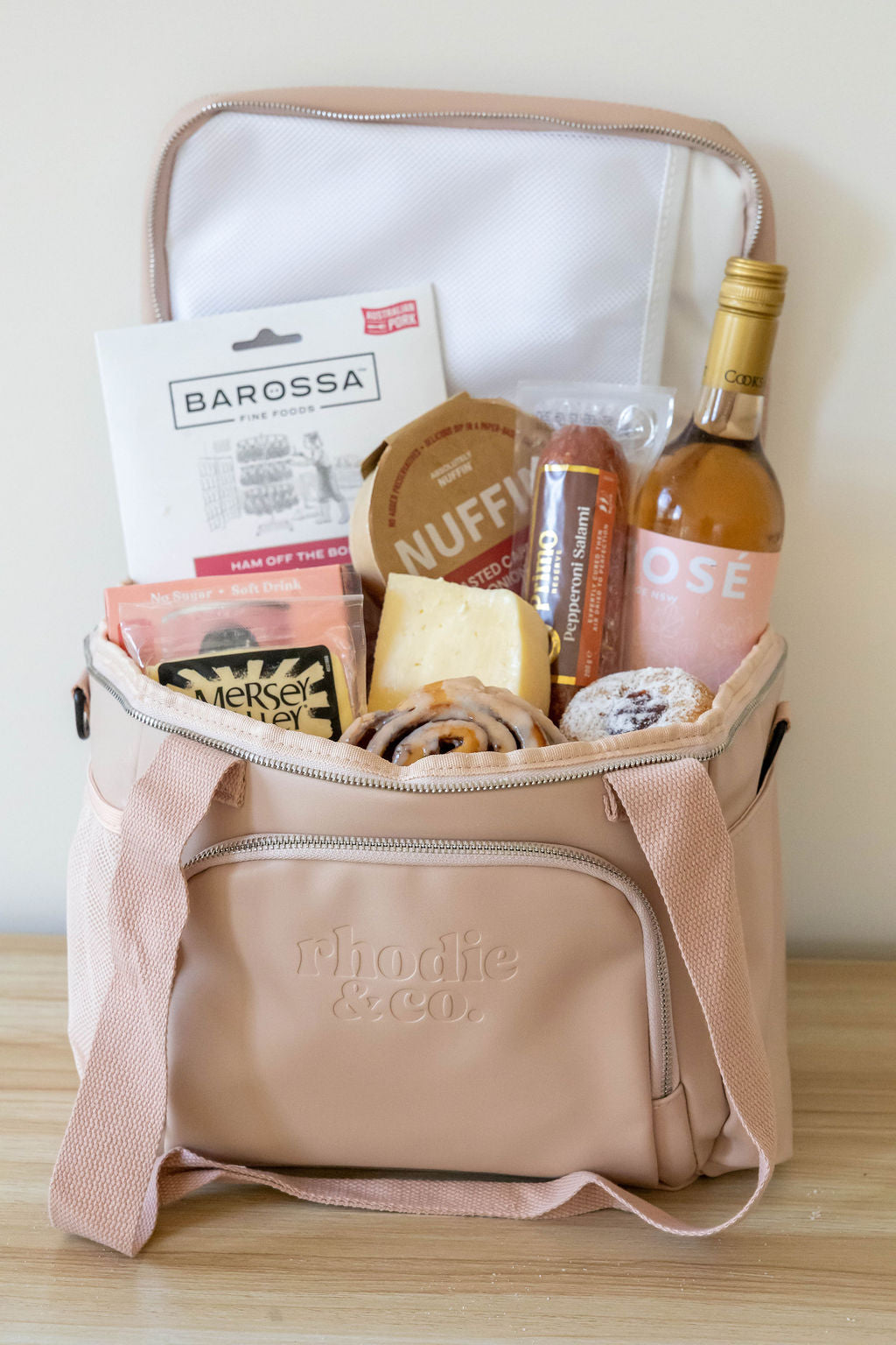 Pink cooler bag with snacks and a bottle of wine on a wooden surface