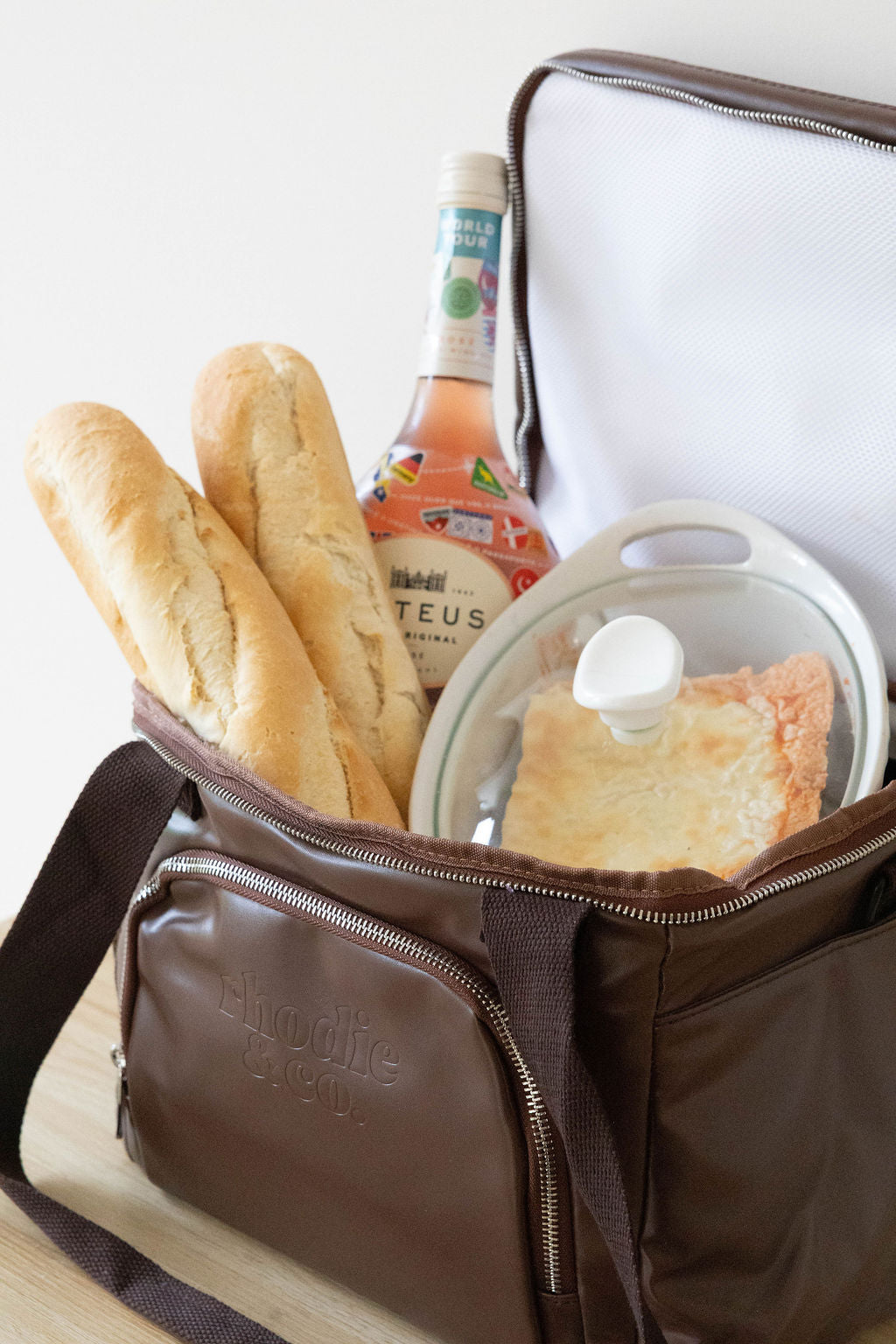 Brown insulated lunch bag with bread, bottle, and pastry on a white background