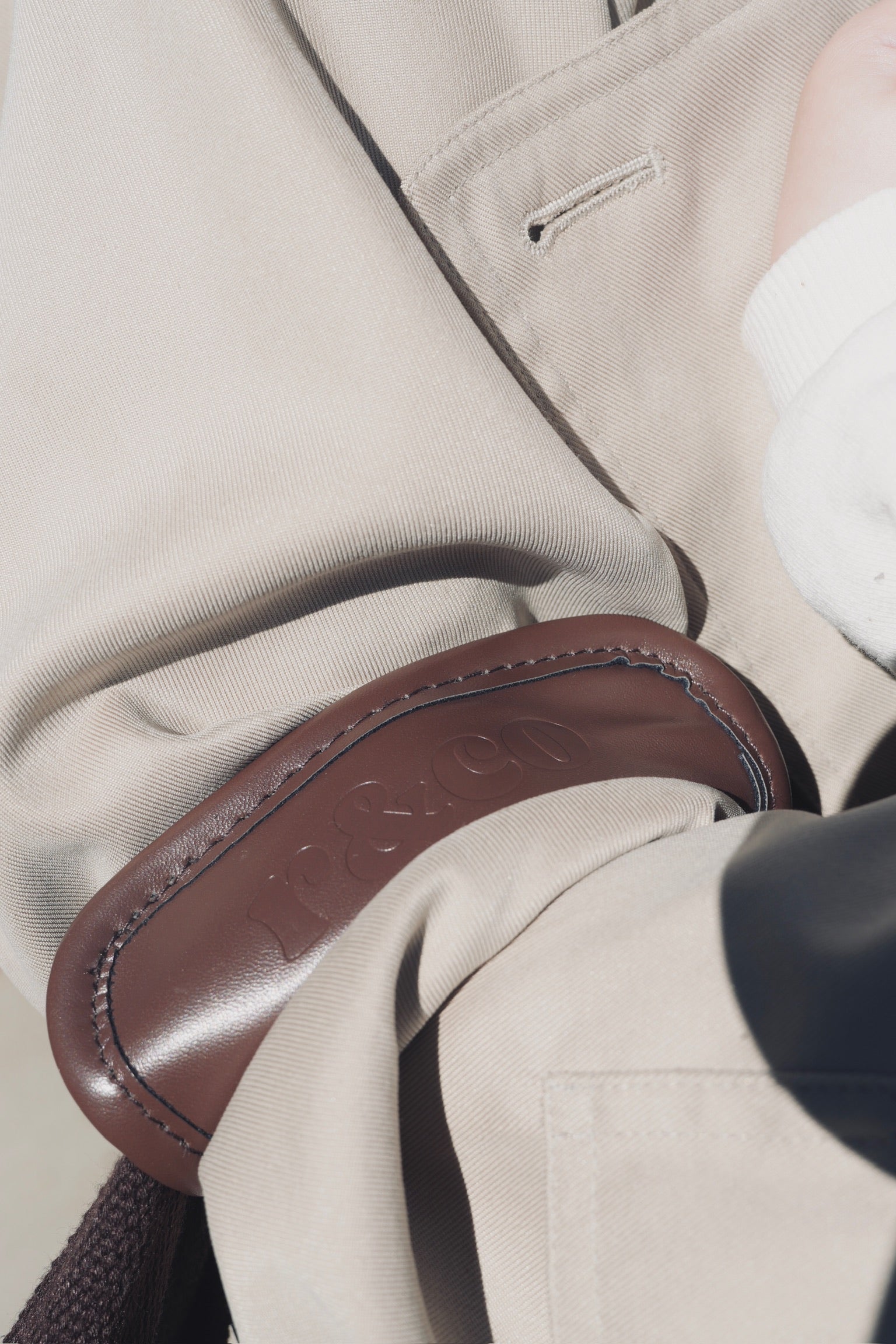 Close-up of a brown leather handle on a beige fabric surface